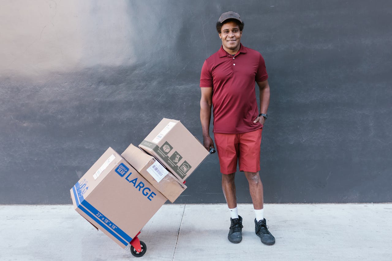 Confident delivery man with packages stacked on a trolley outside, ready for delivery.